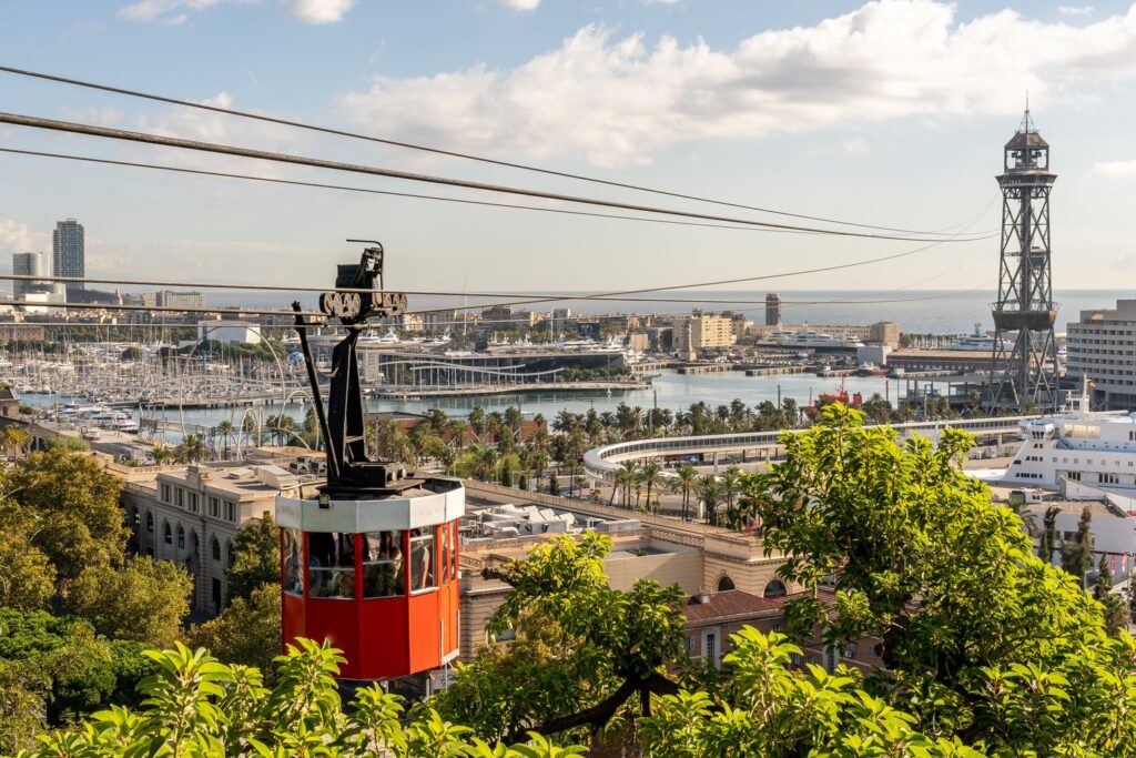 A red cabin of the Port Cable Car swings over the harbour towards Torre Jaume I