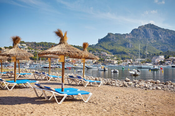 Sun lounges and umbrellas on the main beach of Port de Sóller, with the mountains of the Serra de Tramuntana in the background