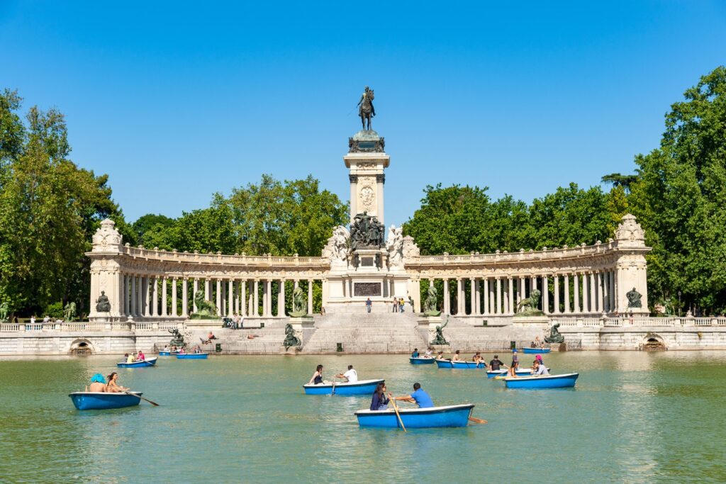 Rowing boats glide across the Great Pond in Retiro Park below the monument to Alfonso XII.